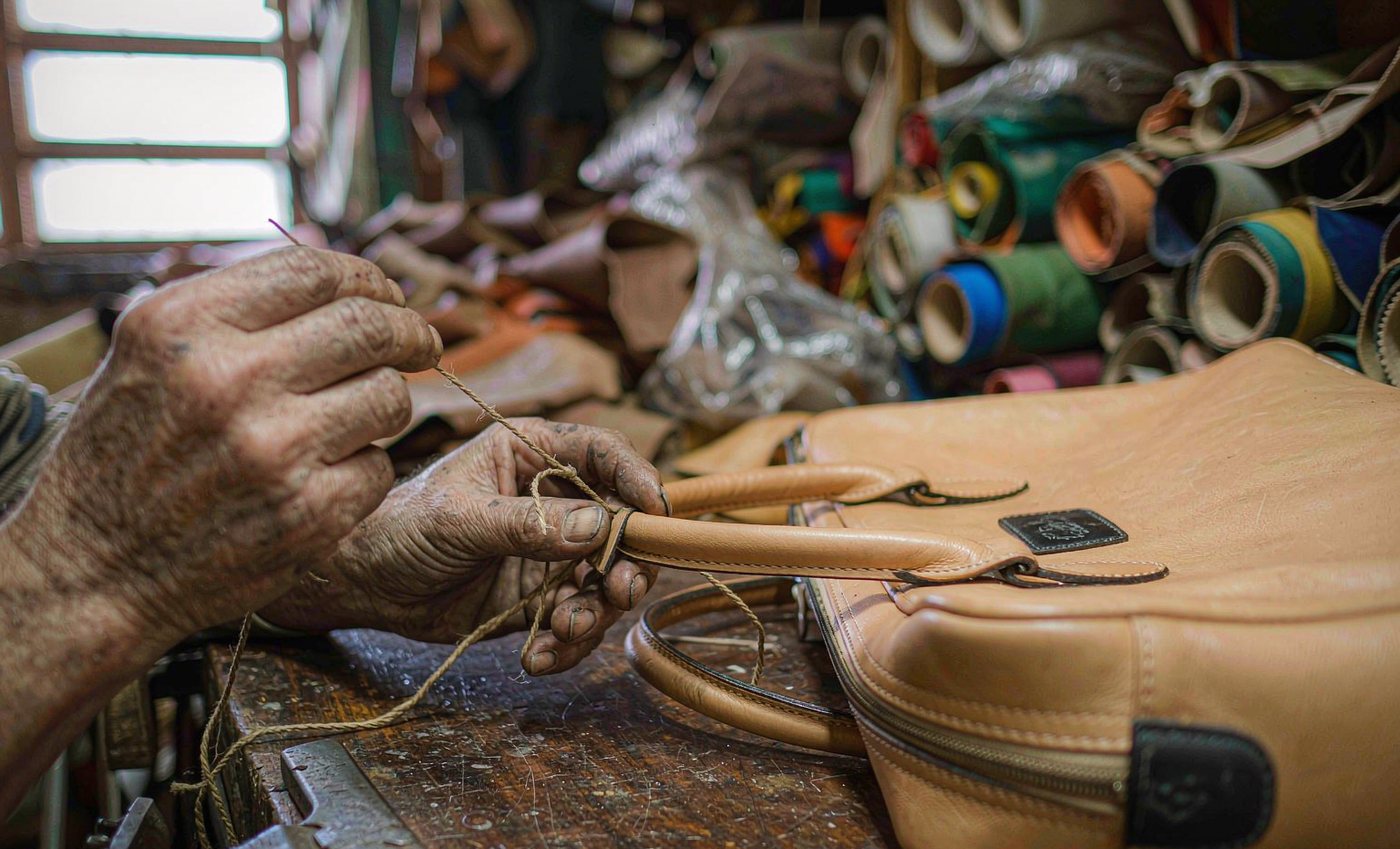 Artisan hand-stitching a tan leather handbag in the AVELINE workshop